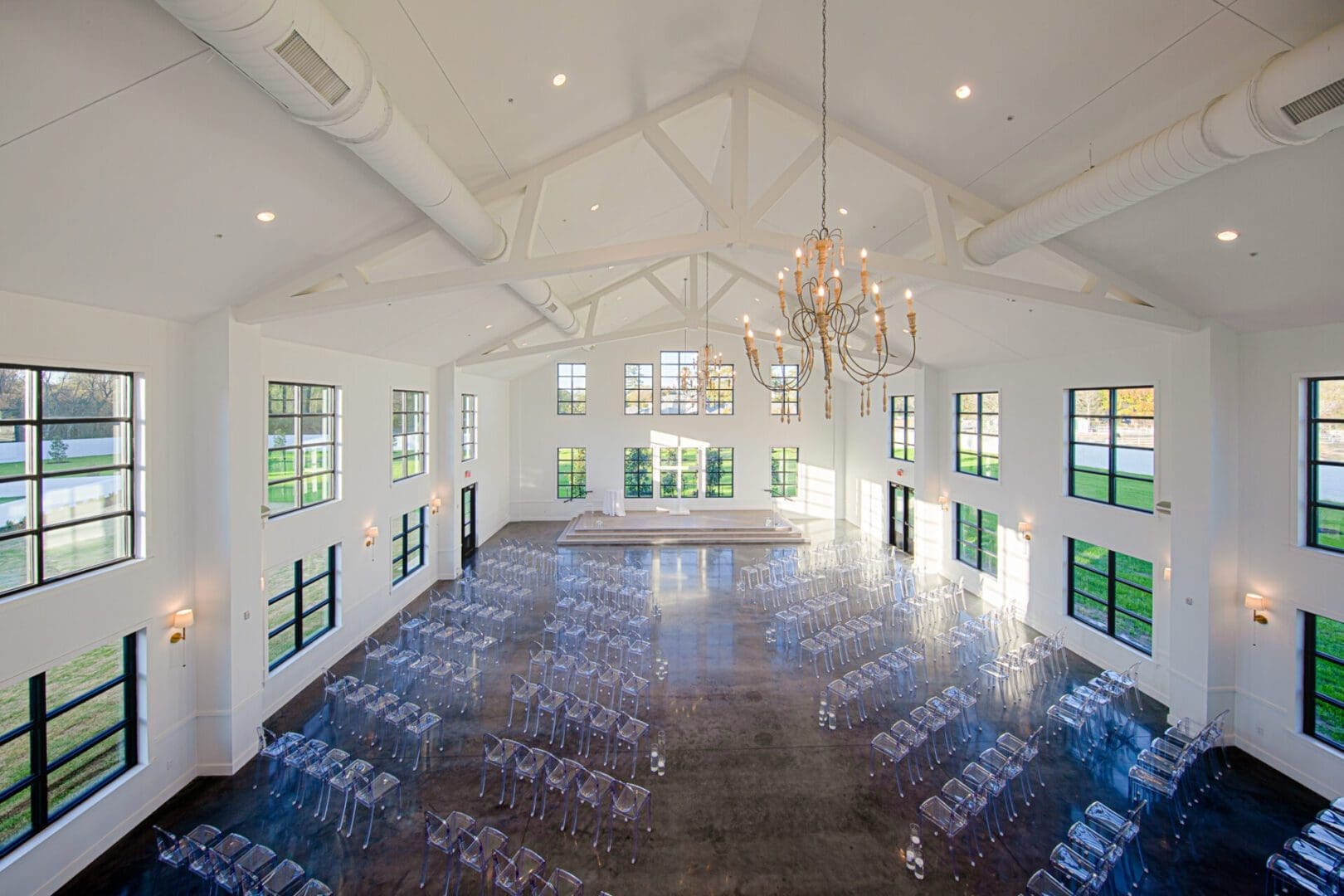 Spacious hall with chandeliers and clear chairs.