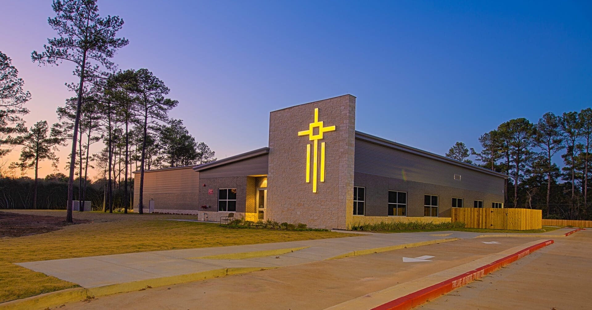 Church building with illuminated cross at dusk.