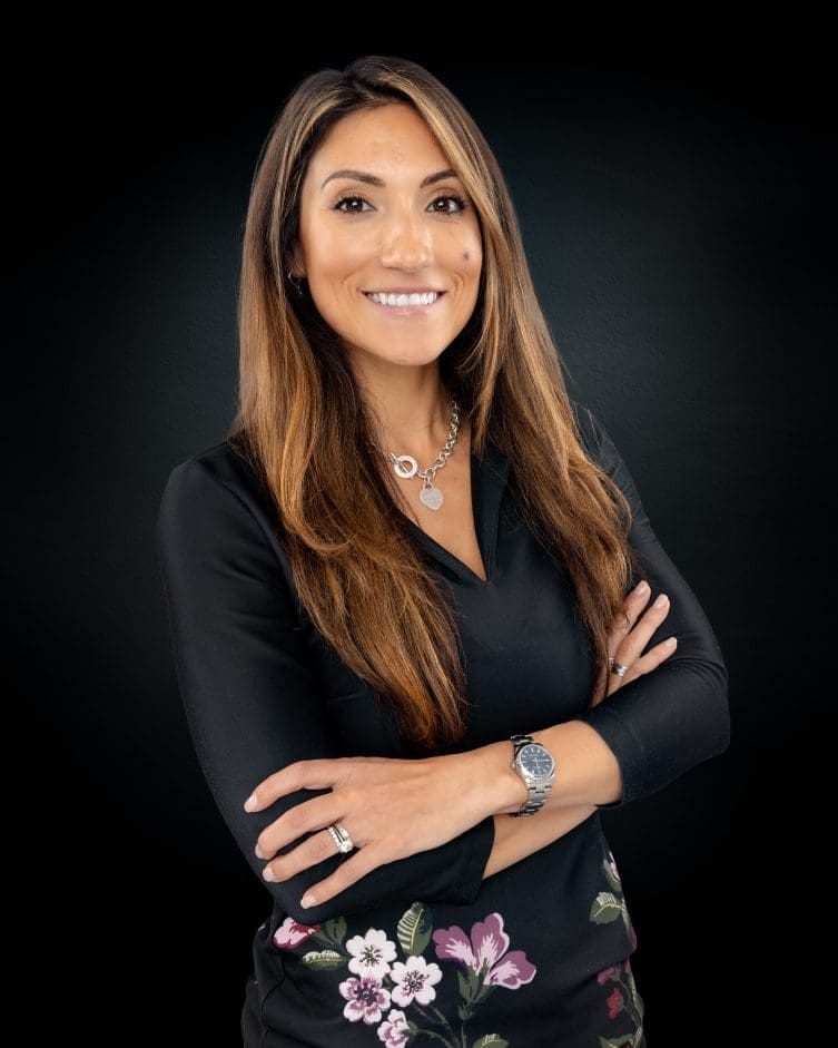 Smiling woman with crossed arms, floral pants.