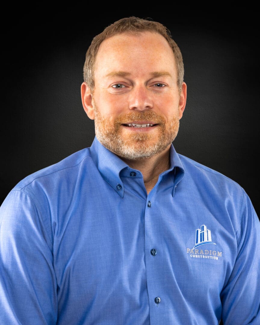 Man in blue shirt, smiling against black background.